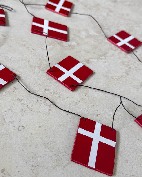 SALUT flaggrekke med Dannebrog-flagg i rødt skinn på svart snor lagt på lys steinoverflate