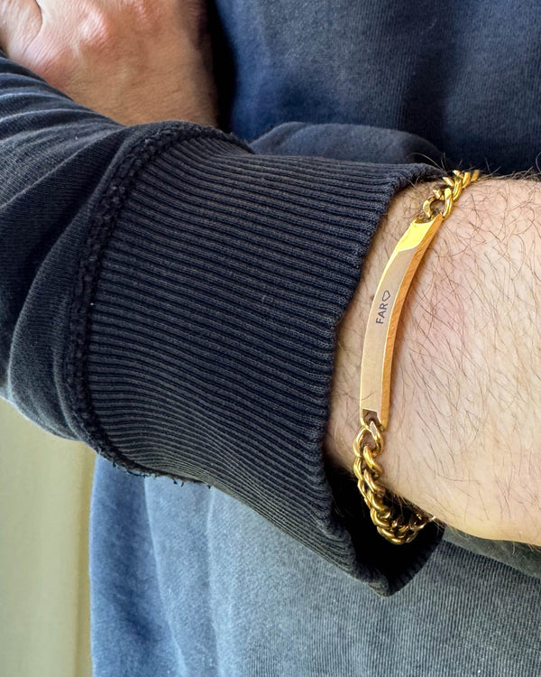ARA armbånd i gullbelagt stål med graveringen "Far" ♡ rundt et mannshåndledd, svart sweatshirt