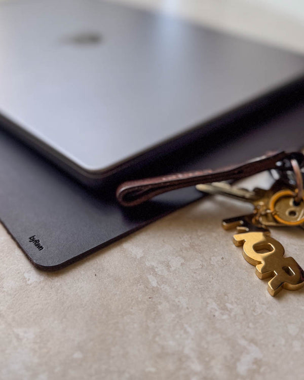 DESK skriveunderlag i mørkebrunt skinn under laptop med nøkkelring i skinn og gullfarget nøkkelanheng