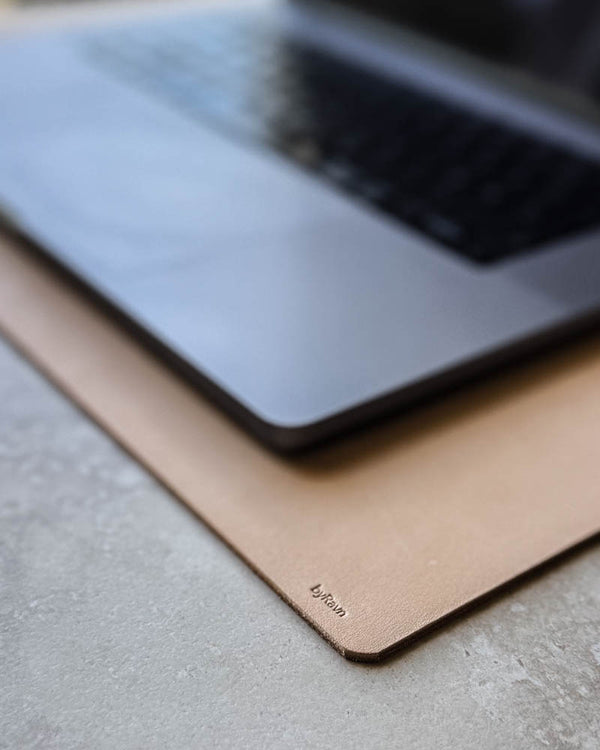 DESK skriveunderlag i naturfarget kjerneskinn med byRavn-preg under laptop på lys bordplate