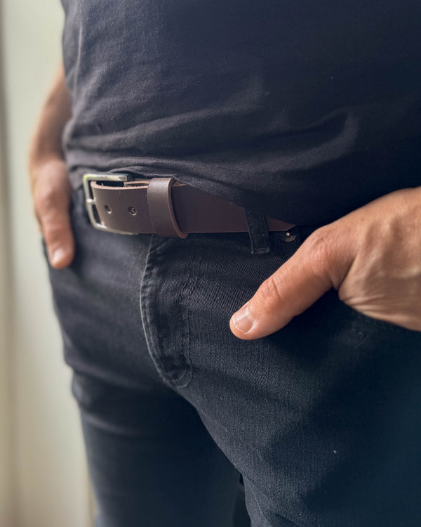 EDGE belte i mørkebrunt skinn båret i svarte jeans med svart t-skjorte og hånden i lommen