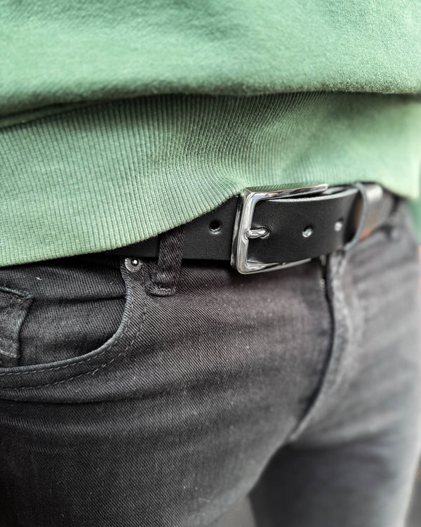 EDGE belte i svart skinn med sølvfarget stålspenne båret i svarte jeans med grønn sweatshirt