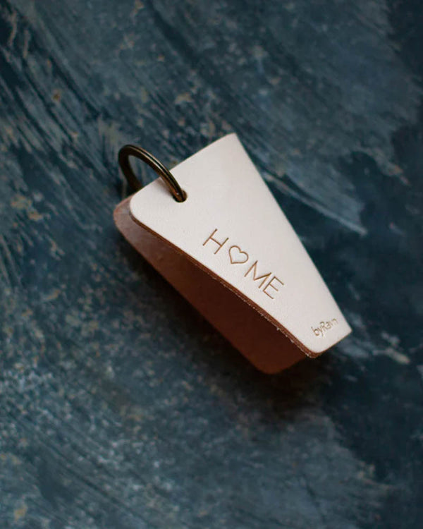 FOLD nøkkelskjuler i naturfarget skinn med graveringen "Home" med hjerte som O, liggende på blå patinert overflate
