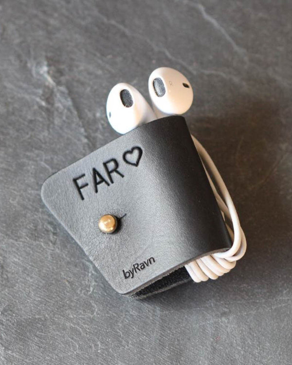 KAX hodetelefonholder i svart skinn med personlig gravering "Far" ♡ og messingknapp, med earpods på mørk skifer