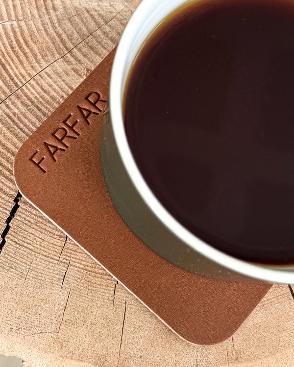 MOKKA firkantet glassbrikke i cognac skinn med graveringen "Farfar" under kopp med kaffe på treskive