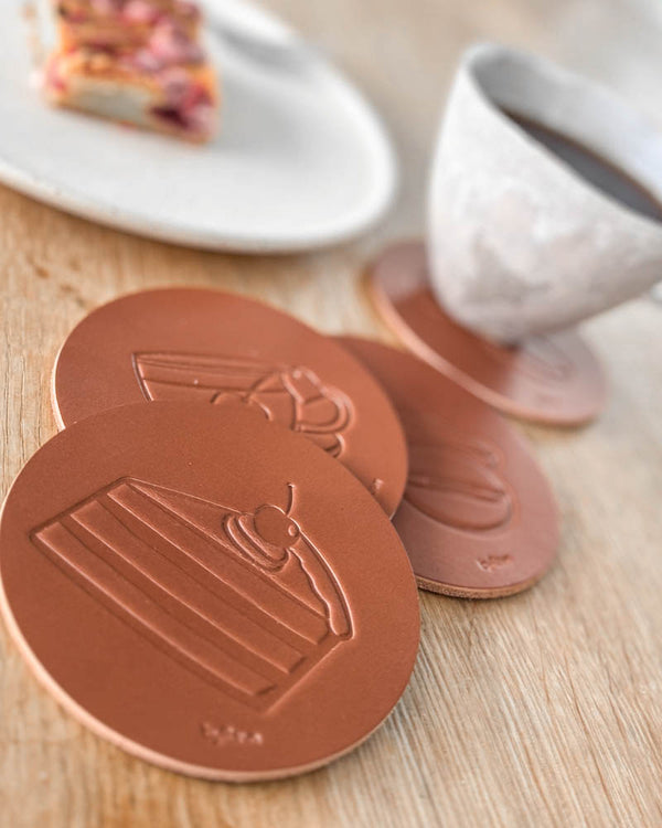 MOKKA kaffe & kake-glassbrikker i cognac skinn preget med bløtkake, ved kaffekopp og tallerken med kake på trebord