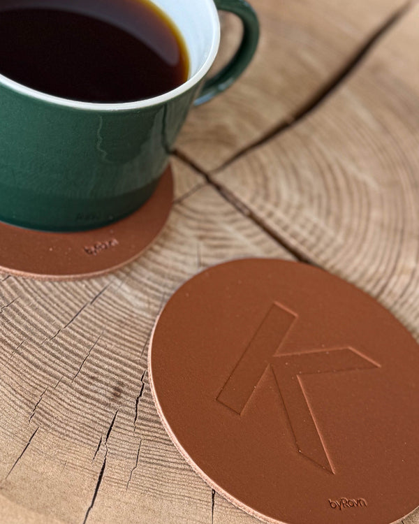 MOKKA glassbrikke i cognac skinn preget med bokstaven "K" på treskive ved grønn kaffekopp på glassbrikke