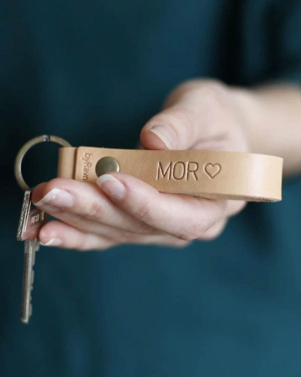 RAVN nøkkelring i naturfarget skinn med graveringen "Mor" ♡, holdt i hånden med nøkler