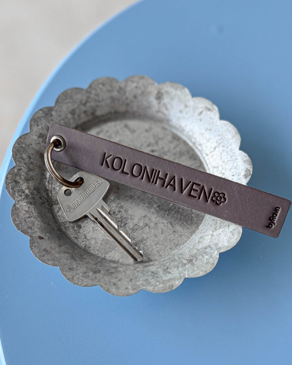 SOLO Large nøkkelring i mørkebrunt skinn med graveringen "Kolonihaven" og blomst, med nøkkel i sinkskål