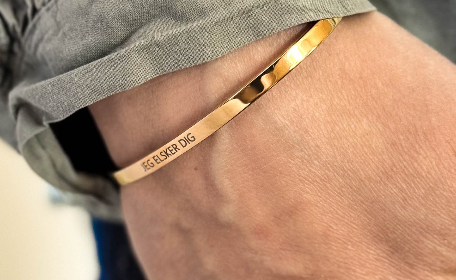 Smykker med handwriting – armbånd i guldbelagt stål med graveringen "Jeg elsker dig" om håndleddet, grå skjorte