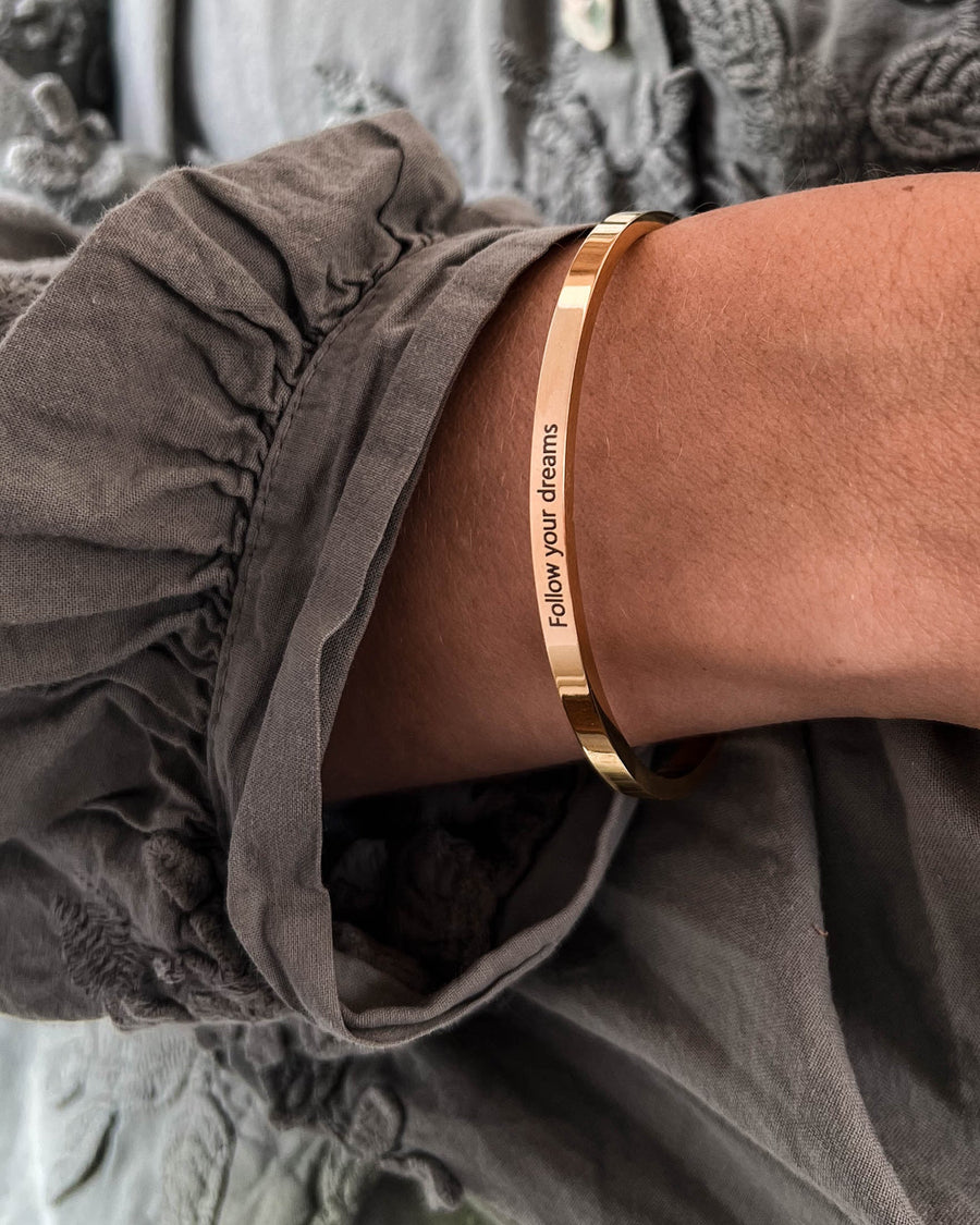 VENUS armbånd i gullbelagt stål med graveringen "Follow your dreams" båret rundt håndleddet