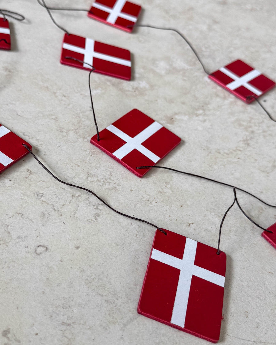 SALUT flaggrekke med Dannebrog-flagg i rødt skinn på svart snor lagt på lys steinoverflate