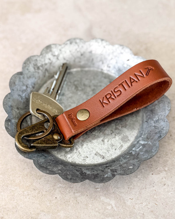 HOOK nøkkelring i cognacfarget skinn gravert med "KRISTIAN" med flysymbol, med nøkkel i en metallskål