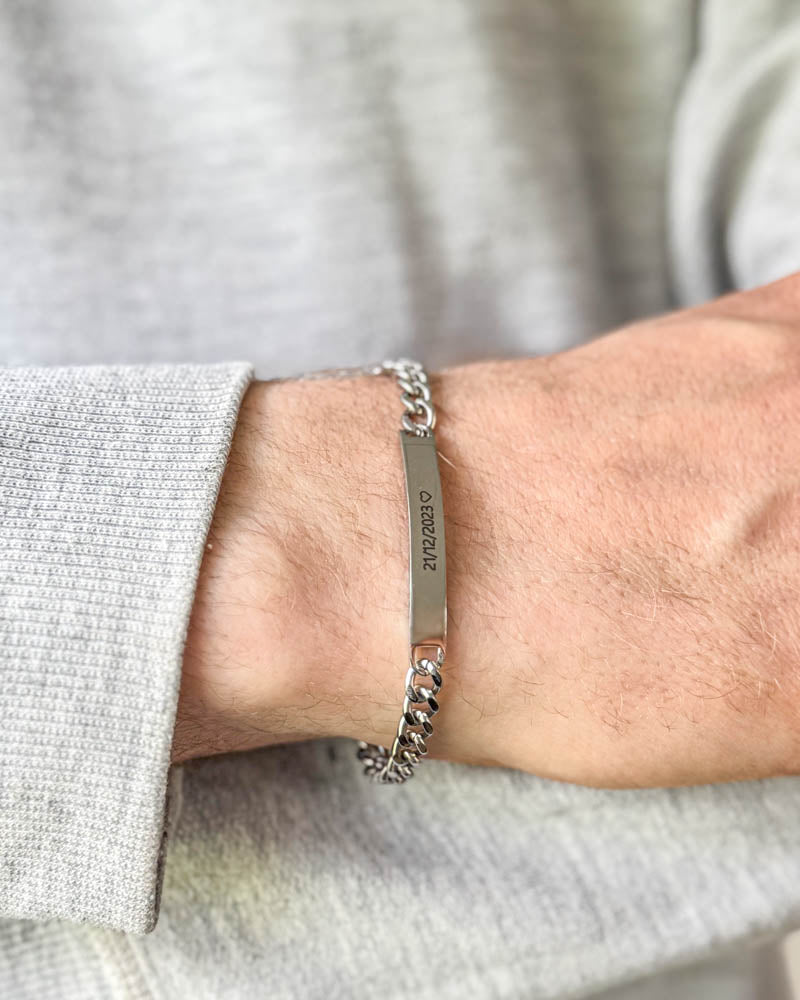 ARA armbånd i sølvfarget rustfritt stål med datoen "21/12/2023" ♡ gravert, båret rundt håndleddet til lysegrå sweatshirt
