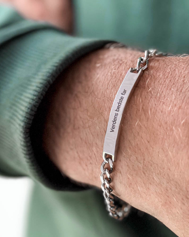 ARA armbånd i sølvfarget rustfritt stål med graveringen "Verdens bedste far" rundt et mannshåndledd, grønn sweatshirt