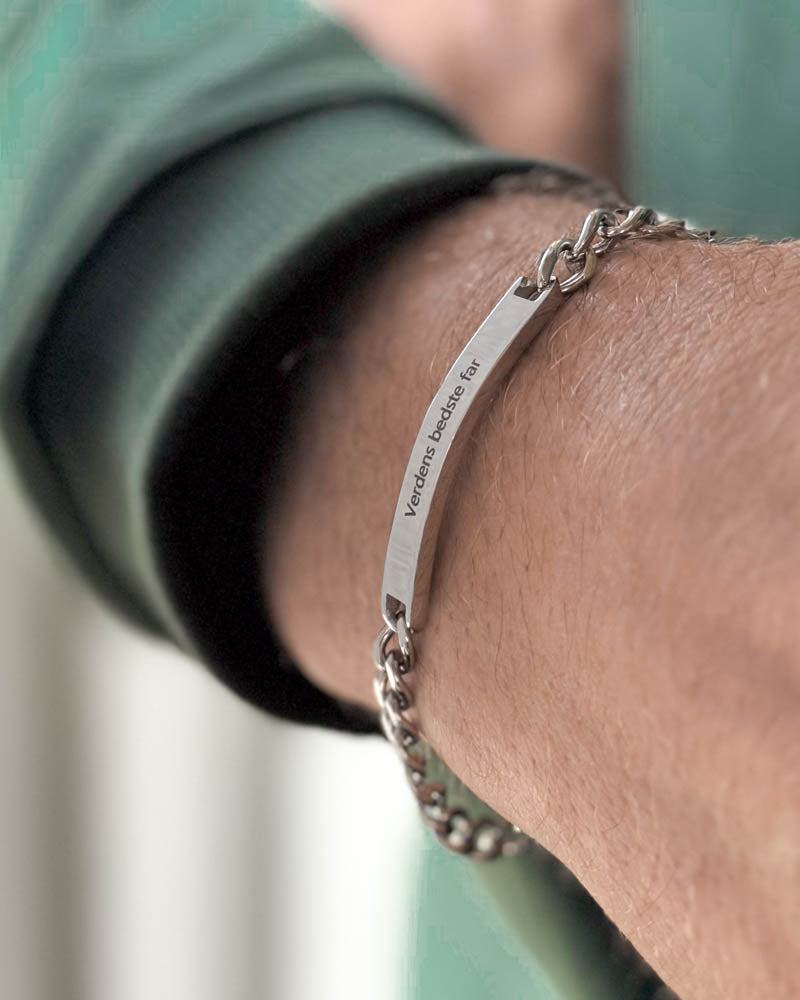 ARA armbånd i sølvfarget rustfritt stål med "Verdens bedste far" gravert på avlang plate, sett på skrå rundt håndleddet