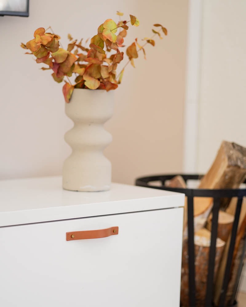 BAND håndtak i cognac skinn på hvit kommode med beige vase med høstgreiner og vedkurv ved siden av