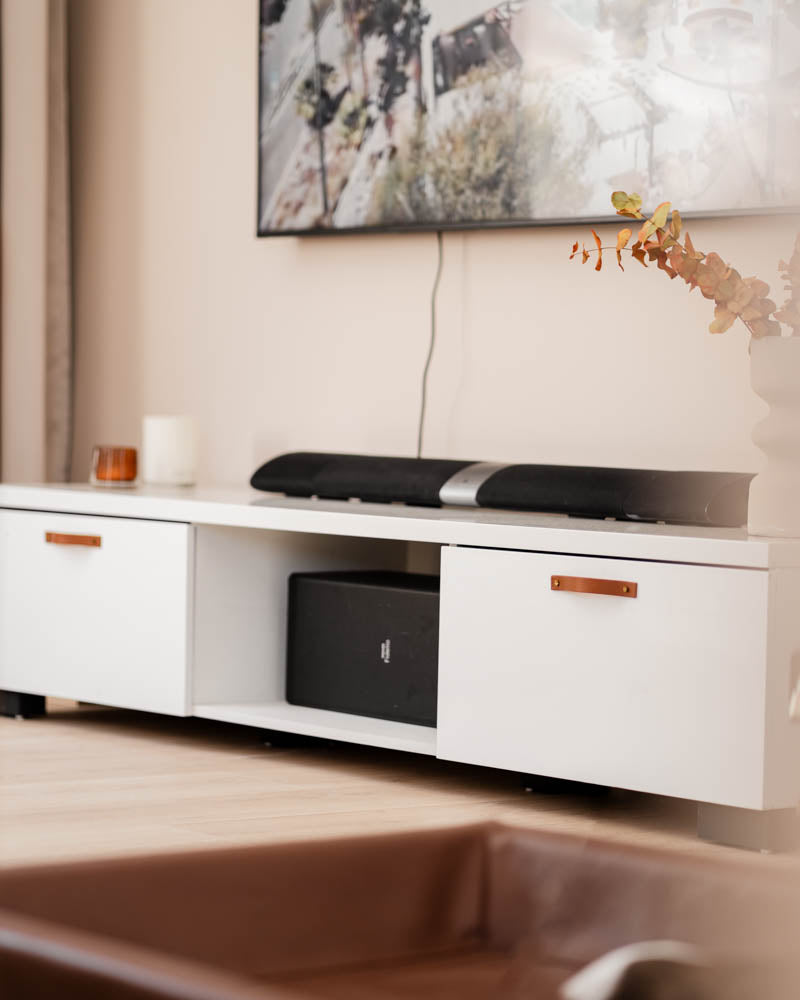 BAND håndtak i cognac skinn på hvit tv-benk med to skuffer, soundbar og tv på veggen i stuen