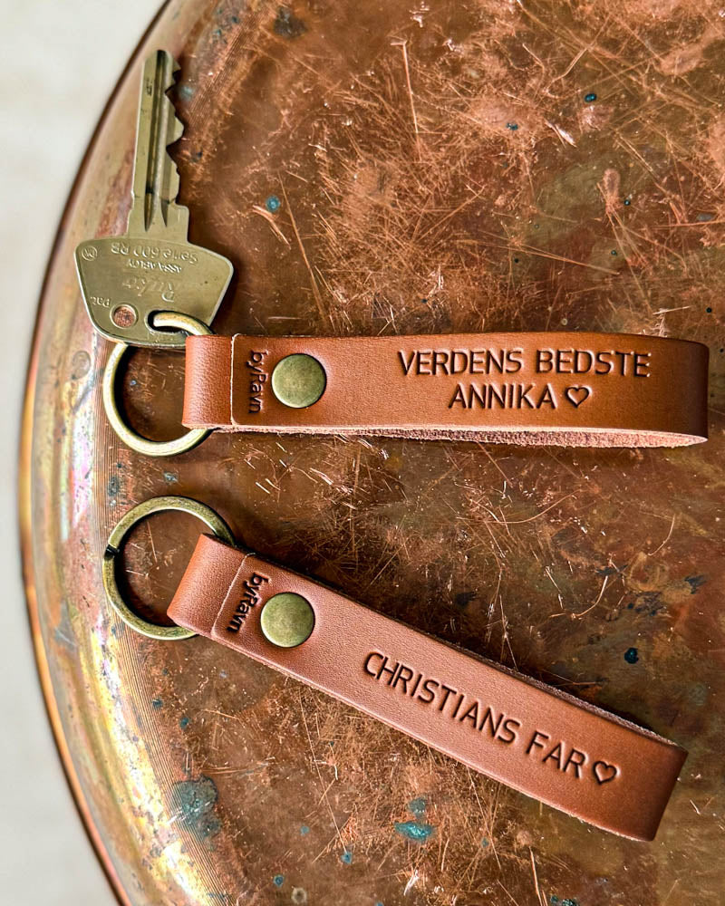To BOND nøkkelringer i cognac skinn med "Verdens bedste Annika" ♡ og "Christians far" ♡ gravert, på kobberbrett med nøkkel