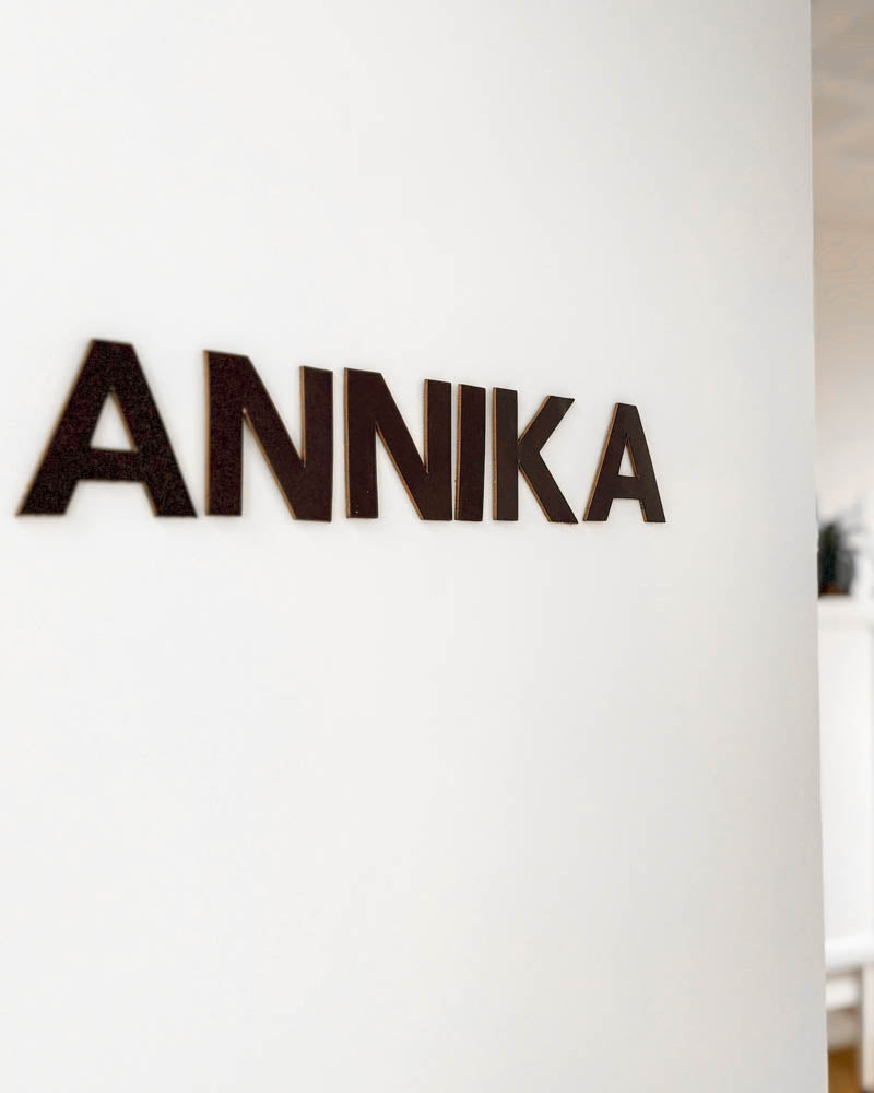 BOX bokstaver i mørkebrunt skinn med navnet "Annika" montert på hvit vegg