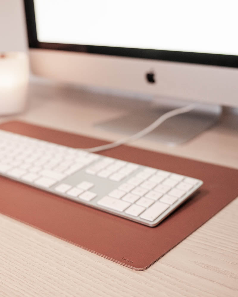 DESK skriveunderlag i cognac skinn under hvitt tastatur foran iMac på lyst treskrivebord