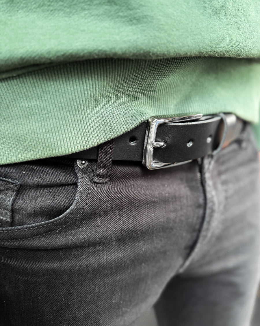 EDGE belte i svart skinn med sølvfarget stålspenne båret i svarte jeans med grønn sweatshirt