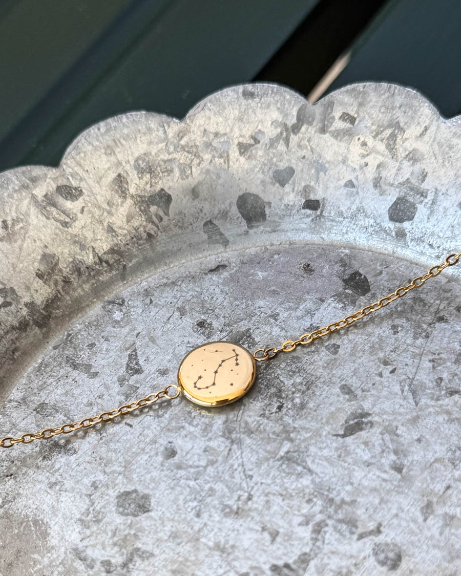 IBI STAR armbånd i gullbelagt stål med stjernebildet Skorpionen gravert på rund plate, liggende på sinkfat