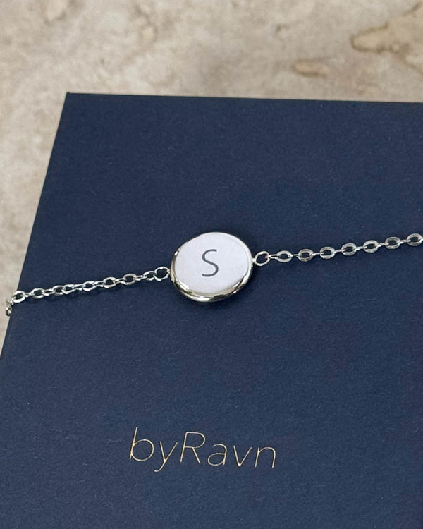 IBI LETTER armbånd i sølvfarget rustfritt stål med bokstaven "S" gravert, liggende på mørkeblå byRavn smykkeeske