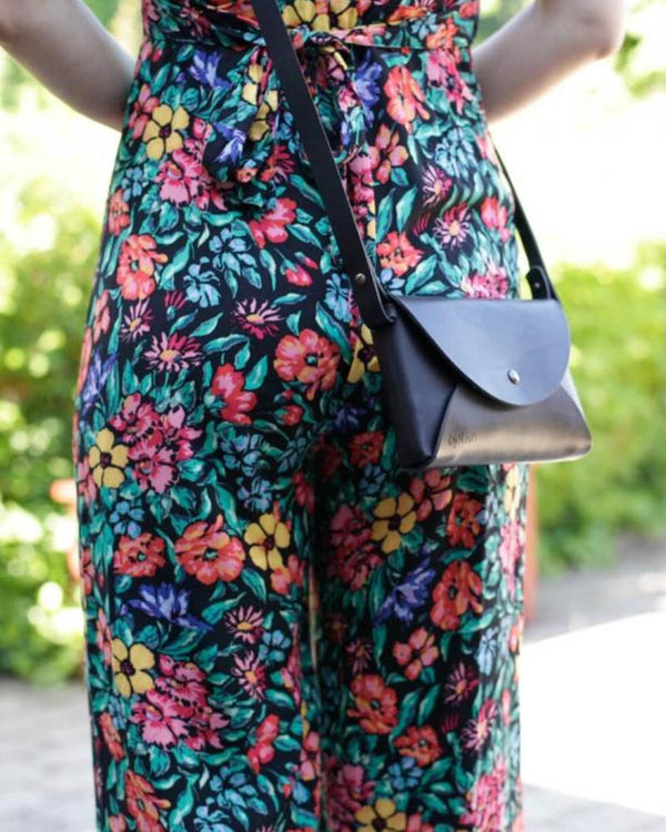 INA skulderveske i svart skinn båret crossbody til blomstrete buksedress i hagen