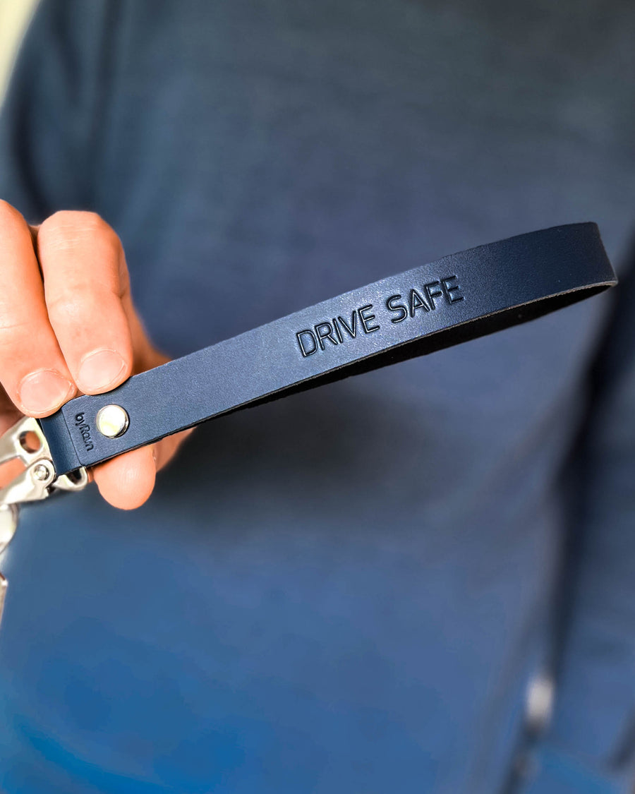 IRON nøkkelring i mørkeblått skinn med lang stropp og graveringen "Drive safe", holdt i hånden