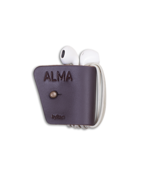 KAX klips til hodetelefoner fra byRavn i mørkebrunt skinn med hodetelefoner viklet rundt og graveringen "Alma"