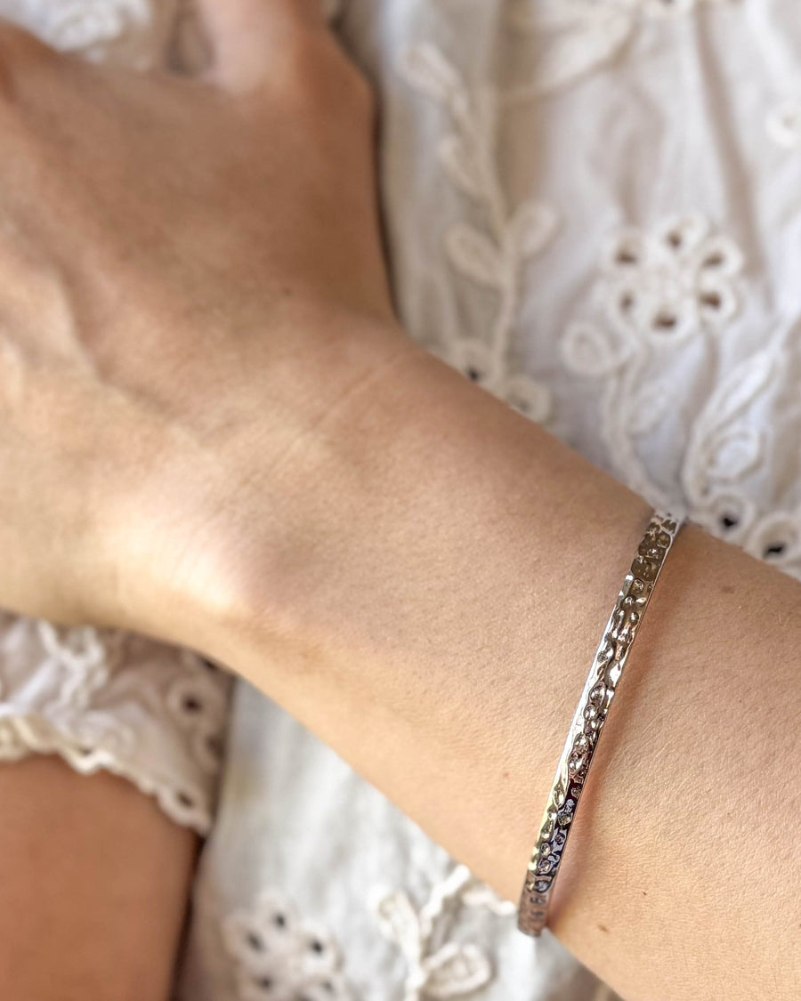 LUNA armbånd i sølvfarget rustfritt stål, hamret armring båret rundt håndleddet til hvit blondebluse