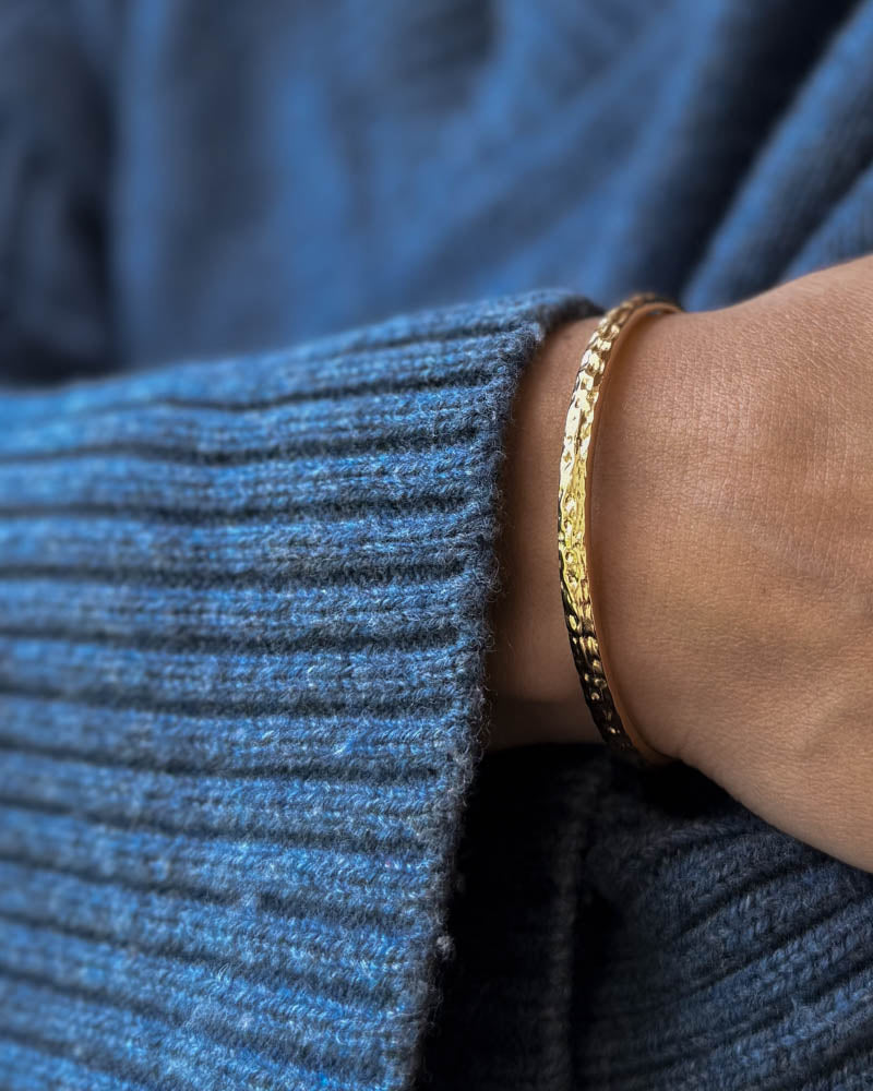LUNA armbånd i gullbelagt stål, hamret armring båret rundt håndleddet til blå strikk