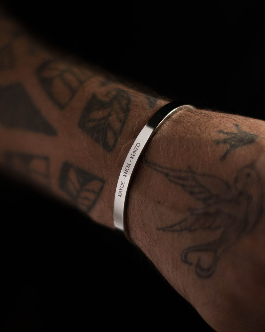 MARS armbånd i sølvfarget rustfritt stål med graveringen "Kaylie – Knox – Kenzo" på tatovert mannsarm