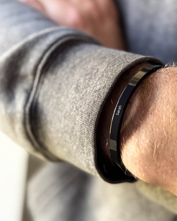 MARS armbånd i svart stål med navnet "Sarah" gravert, rundt et mannshåndledd, grå sweatshirt