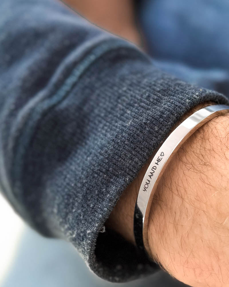 MARS SCRIPT armbånd i sølvfarget rustfritt stål med "You and me" ♡ gravert i håndskrift rundt håndleddet, blå sweatshirt