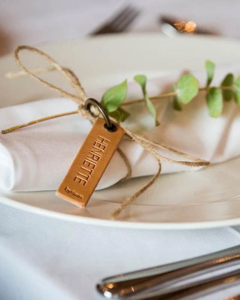 MERRY bordkort i naturfarget skinn med navnet "Henriette" gravert, bundet rundt hvit serviett med eukalyptus