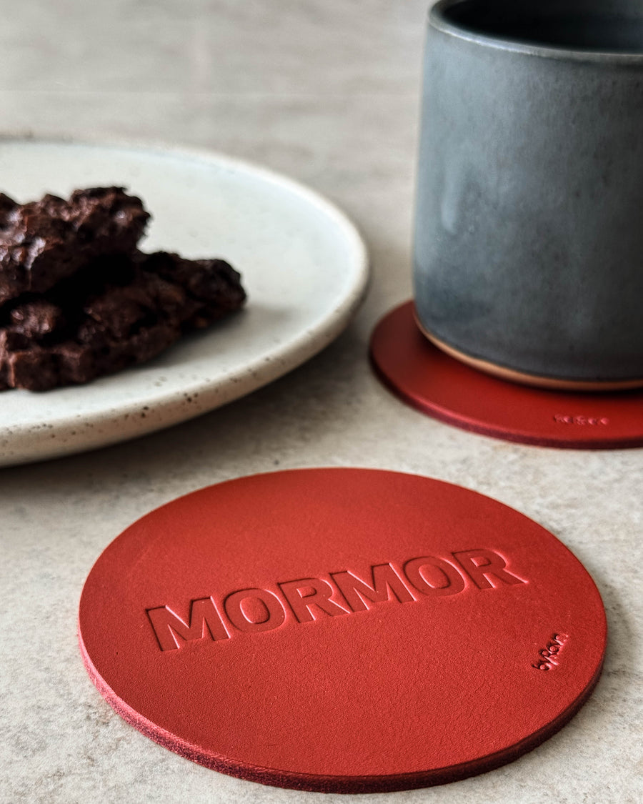 MOKKA glassbrikke i rødt skinn preget "Mormor" på lyst bord med grå kaffekopp og tallerken med sjokoladekake