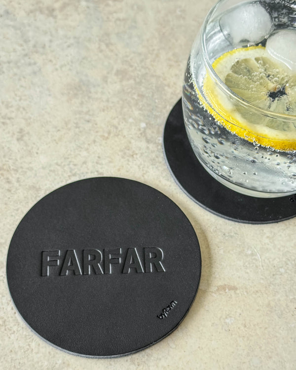 MOKKA glassbrikke i svart skinn preget "Farfar" på lyst bord ved glass med gin og tonic og sitronskive