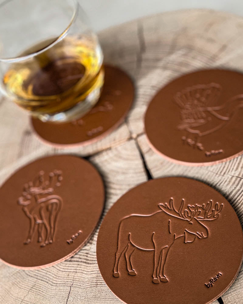 MOKKA jakt-glassbrikker i cognac skinn preget med elg, dåhjort og tiur på treskive ved glass med whisky