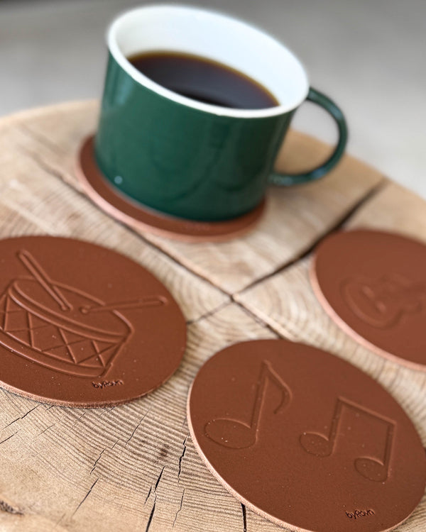 MOKKA glassbrikker i cognac skinn preget med tromme og noter på treskive med grønn kaffekopp