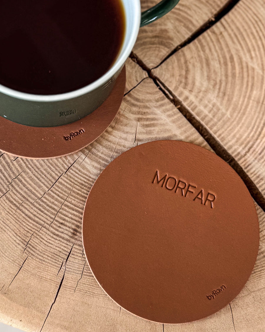 MOKKA rund glassbrikke i cognac skinn med graveringen "Morfar" på treskive ved siden av grønn kaffekopp på glassbrikke