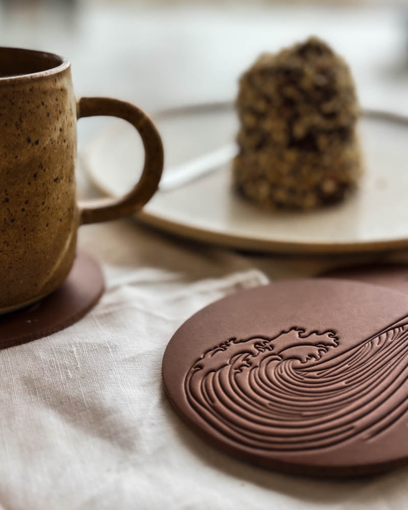 MOKKA sommerhus-glassbrikke i cognac skinn preget med bølgemotiv på linduk ved kaffekopp og tallerken med kake
