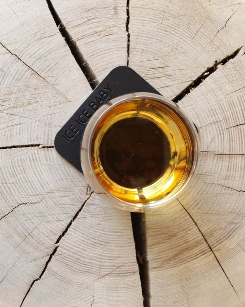 MOKKA firkantet glassbrikke i svart skinn med graveringen "Ice ice baby" under whiskyglass på treskive sett ovenfra