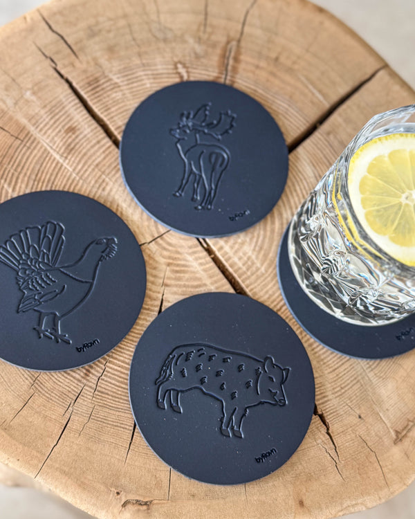 MOKKA jakt-glassbrikker i mørkeblått skinn preget med villsvin, tiur og dåhjort på treskive ved glass med sitronskive