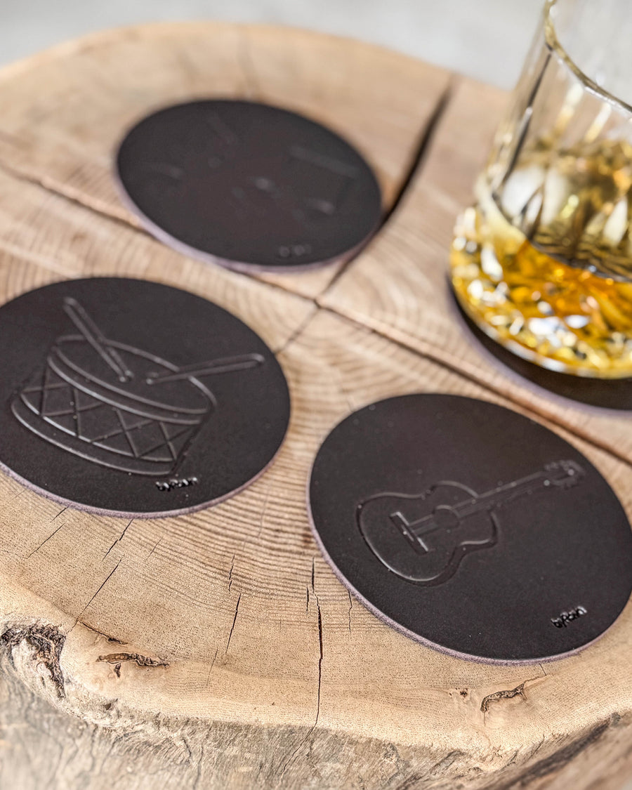 MOKKA glassbrikker i mørkebrunt skinn preget med tromme og gitar på treskive ved krystallglass med whisky