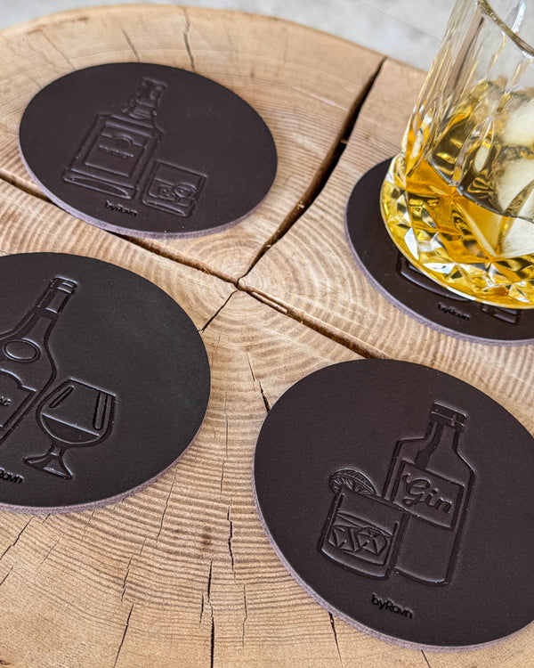 MOKKA brennevin-glassbrikker i mørkebrunt skinn preget med gin, cognac og whisky på treskive ved glass med whisky og is