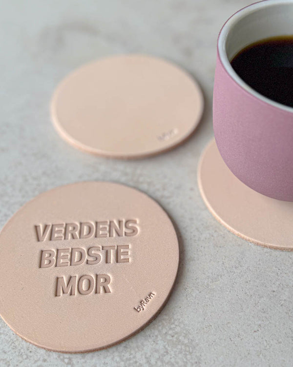 MOKKA glassbrikker i naturfarget skinn preget "Verdens bedste mor" på lyst bord med rosa kaffekopp