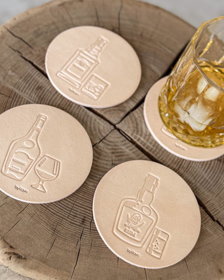 MOKKA brennevin-glassbrikker i naturfarget skinn preget med cognac, rom og whisky på treskive ved glass med whisky og is
