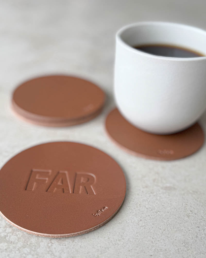 MOKKA glassbrikke i cognac skinn preget "Far" i store bokstaver, flere glassbrikker og hvit kaffekopp bak